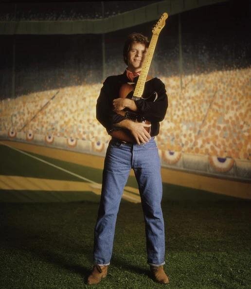 John Fogerty standing on a stadium outfield holding a guitar — the Centerfield-era promo image